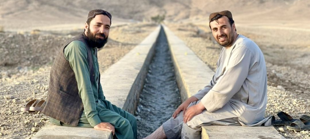 Two men sit across newly installed irrigation canal in Kandahar, Afghanistan